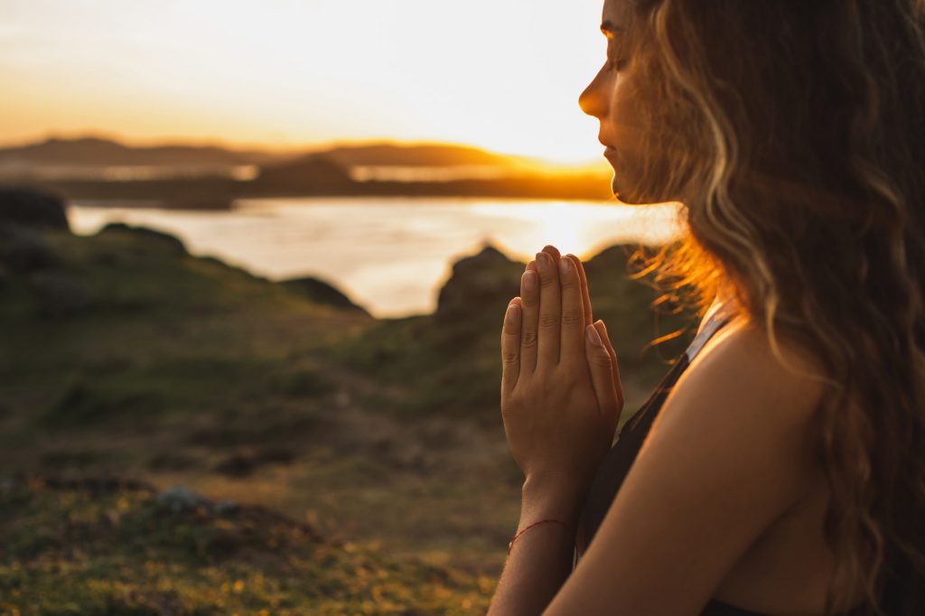 Woman praying alone at sunrise. Nature background. Spiritual and emotional concept.