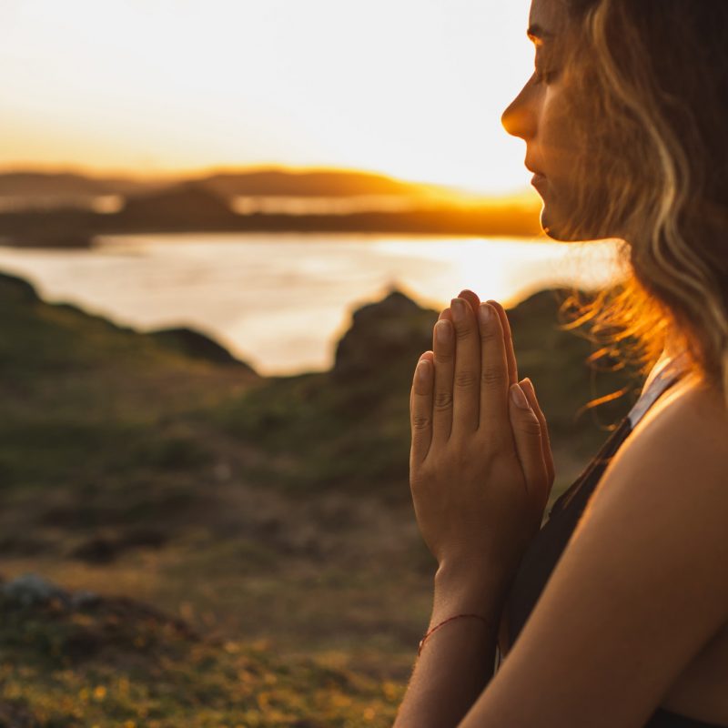 Woman praying alone at sunrise. Nature background. Spiritual and emotional concept.
